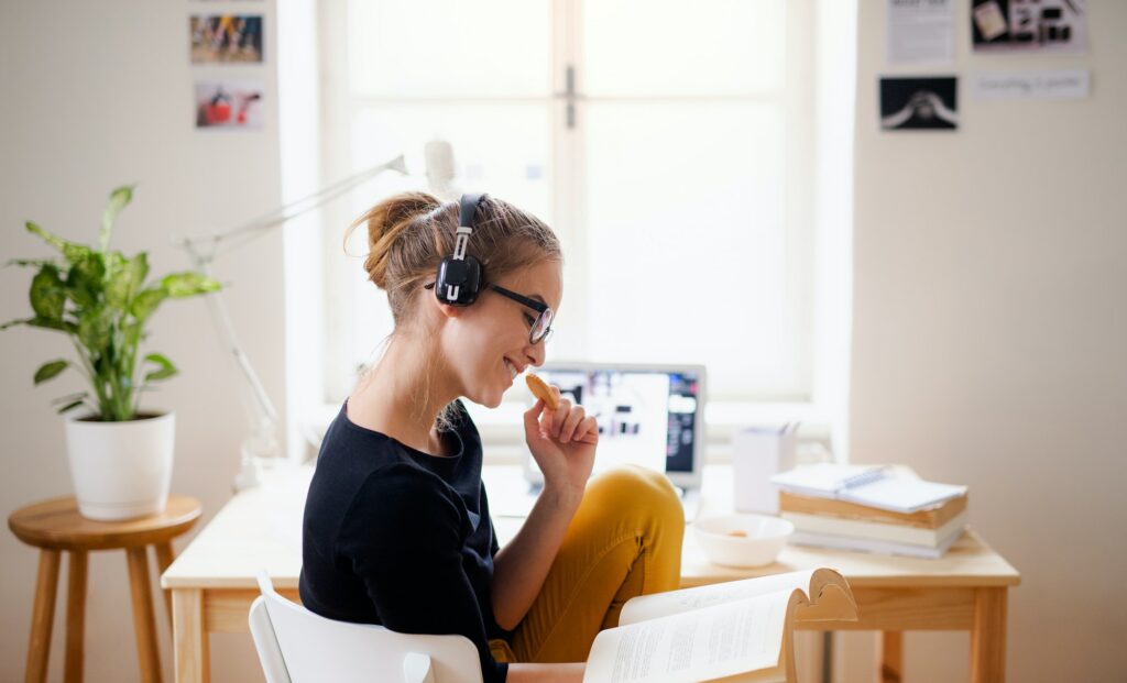A young female student sitting at the table, using headphones when studying