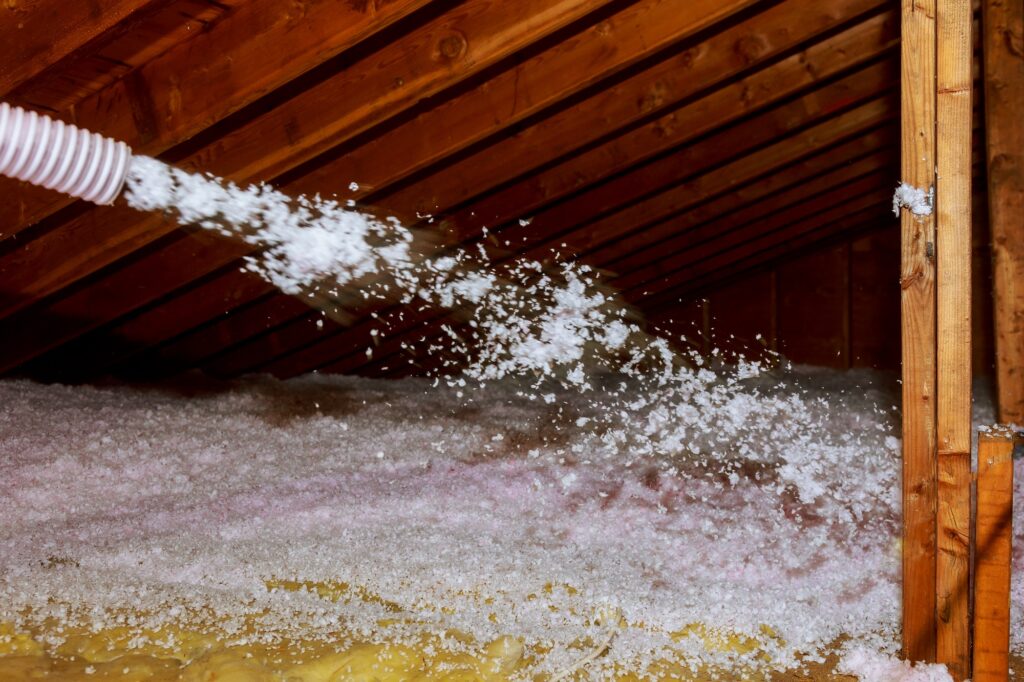 Worker Spraying mineral rock wool of thermal insulation layer under the roof house attic insulation